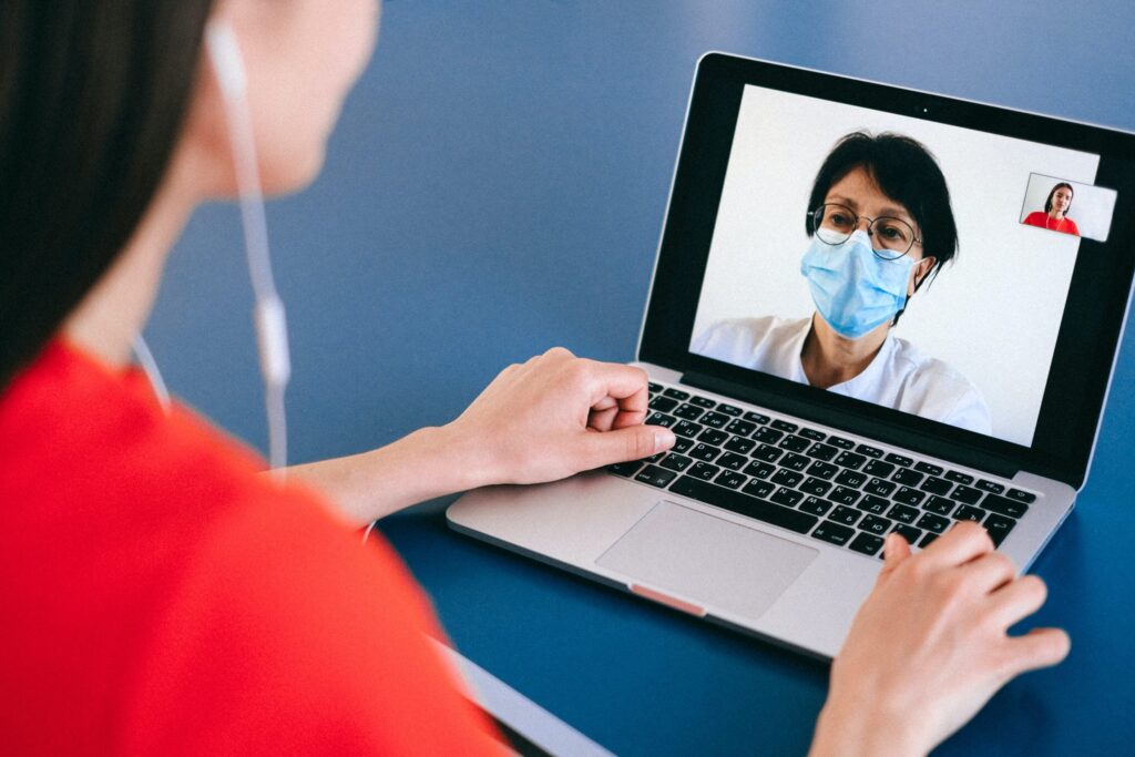 Woman video chatting on laptop with healthcare professional wearing face mask