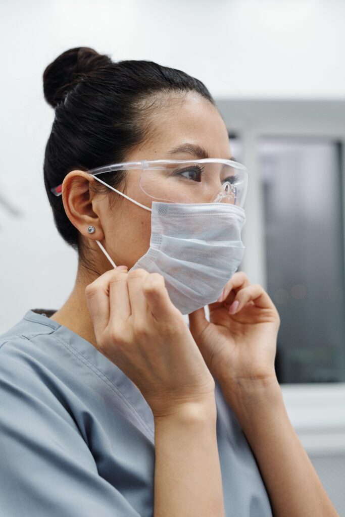 Woman healthcare professional wearing goggles and putting on face mask