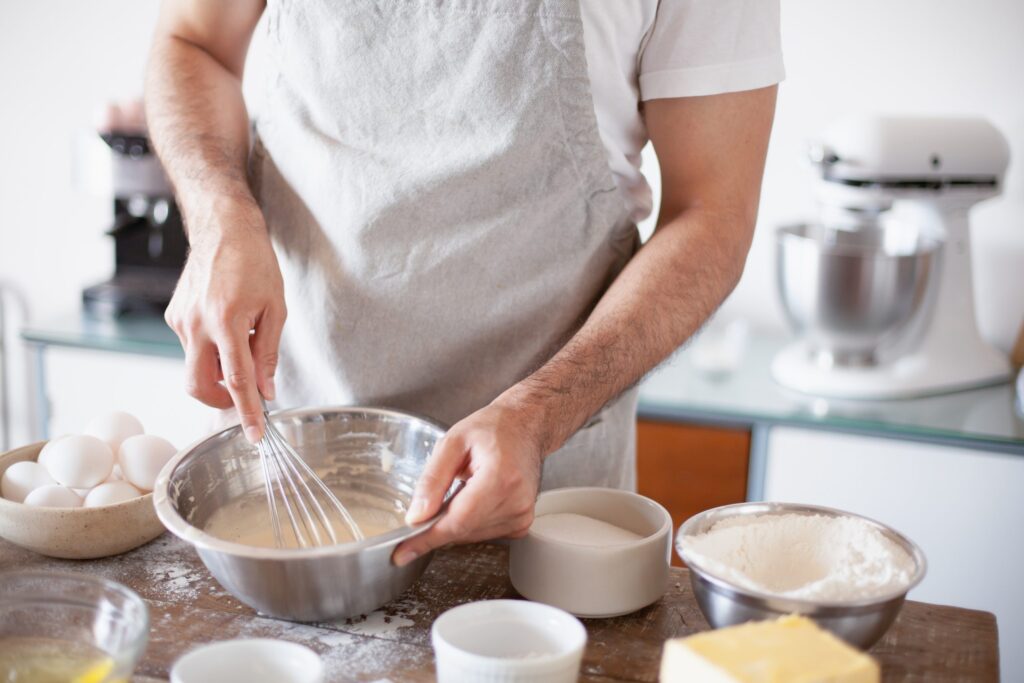 Man wearing apron and whisking eggs and powder